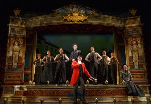 The cast with Bryce Pinkham as Monty Navarro (standing center), Jefferson Mays as Lord Adalbert D'Ysquith (red), and Jane Carr as Miss Shingle (seated) in a scene from "A Gentleman's Guide to Love and Murder" at the Walter Kerr Theater. Photo credit: Joan Marcus.